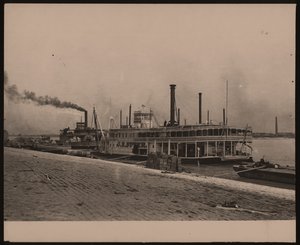 Horizontal, black and white photograph of the steamboat C.R. Suter. Another steamboat is parked behind it and crates are piled on the shore